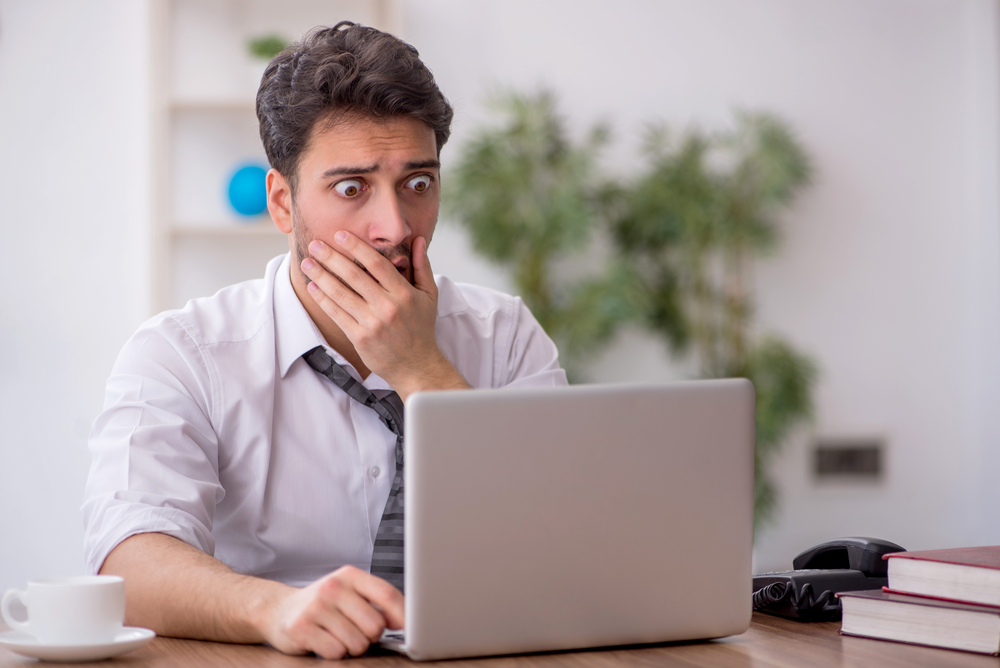 Young male employee looking shocked at the computer